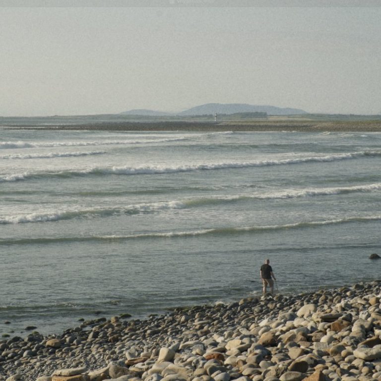 A person walking along Strandhill beach with waves rolling in